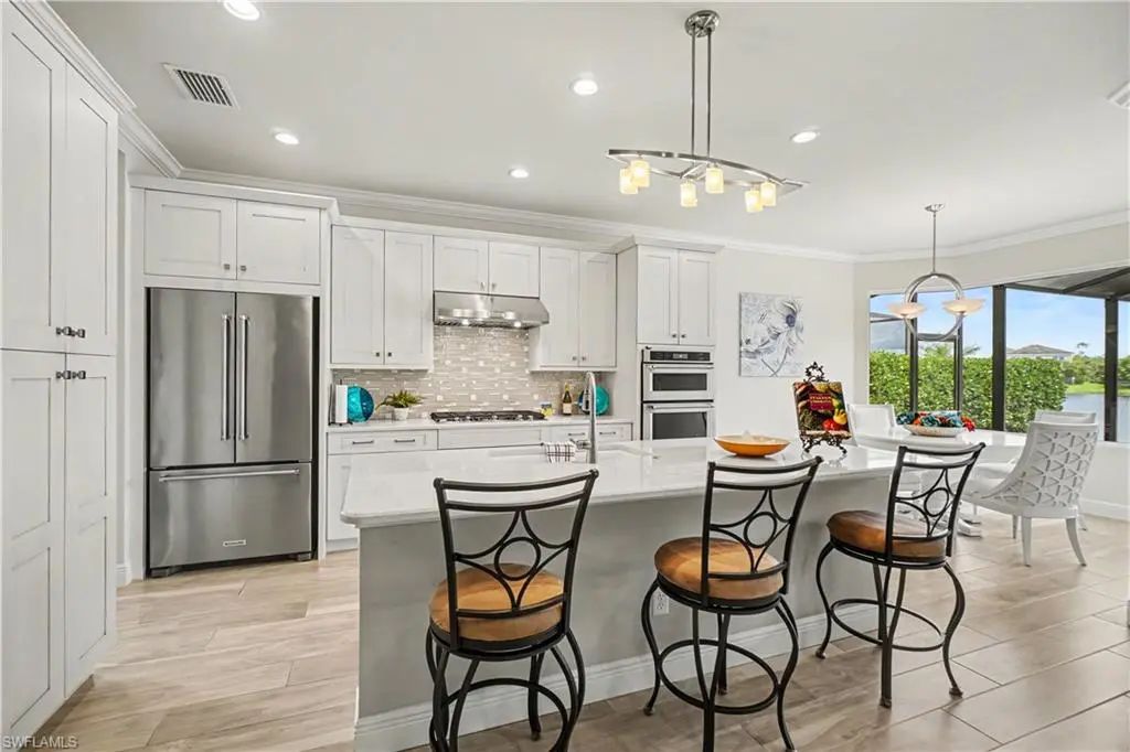 White kitchen with island seating, KitchenAid appliances and gas cooktop at 9062 Montserrat Drive, Naples FL