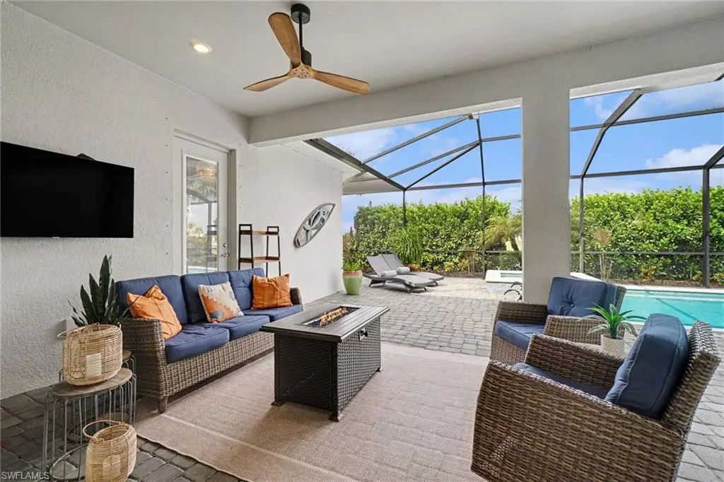 Covered lanai lounge at 15880 Talon Terrace with wicker seating, wall-mounted television and the screened pool beyond